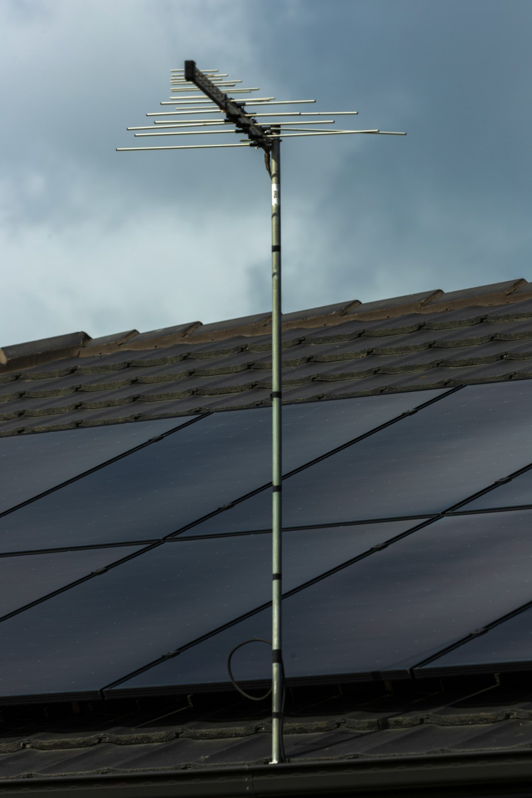 Rooftop solar panels with TV antenna under stormy clouds.